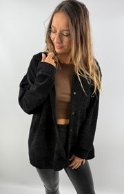 Frau trägt ein schwarzes Cordhemd über einem braunen Top – lässiger, offener Look.