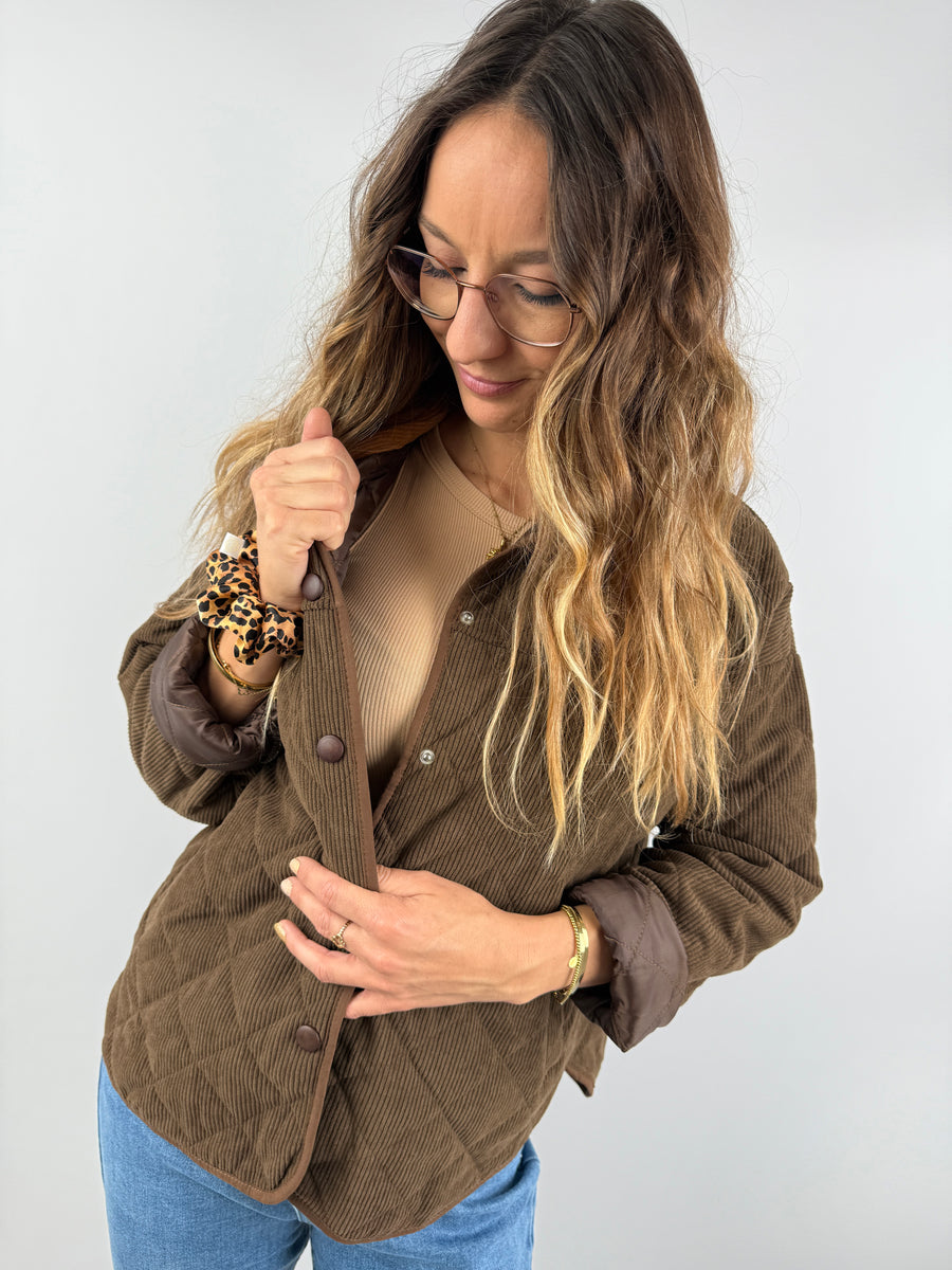 Frau trägt eine braune gesteppte Cordjacke mit Druckknöpfen, kombiniert mit einem beigen Ripp-Top – gemütlicher Look in warmen Naturtönen.