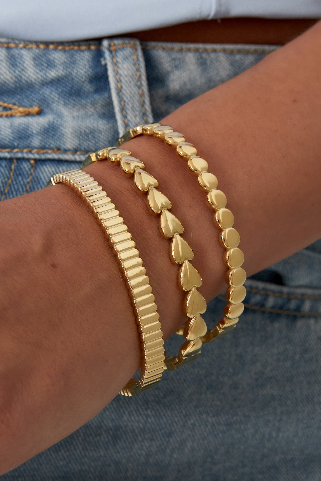 Gestapelter Look am Handgelenk: goldfarbener, fester Armreif mit feiner Gliederstruktur, kombiniert mit zwei weiteren goldenen Armbändern.