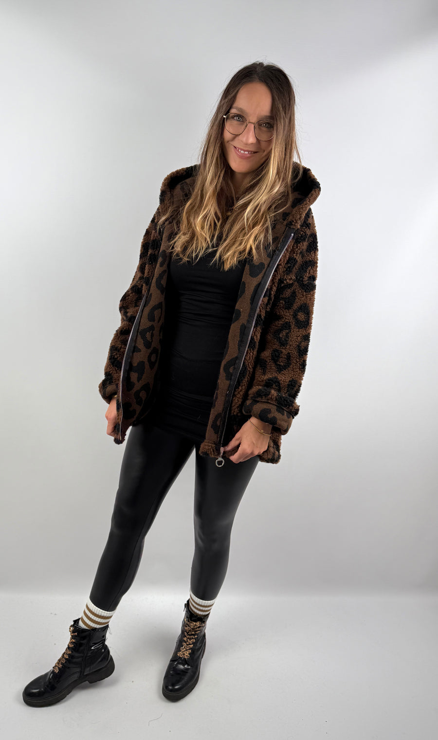 Frau trägt eine dunkelbraune Leo Teddy Jacke mit Leo-Print, kombiniert mit schwarzer Lederleggings und Boots.