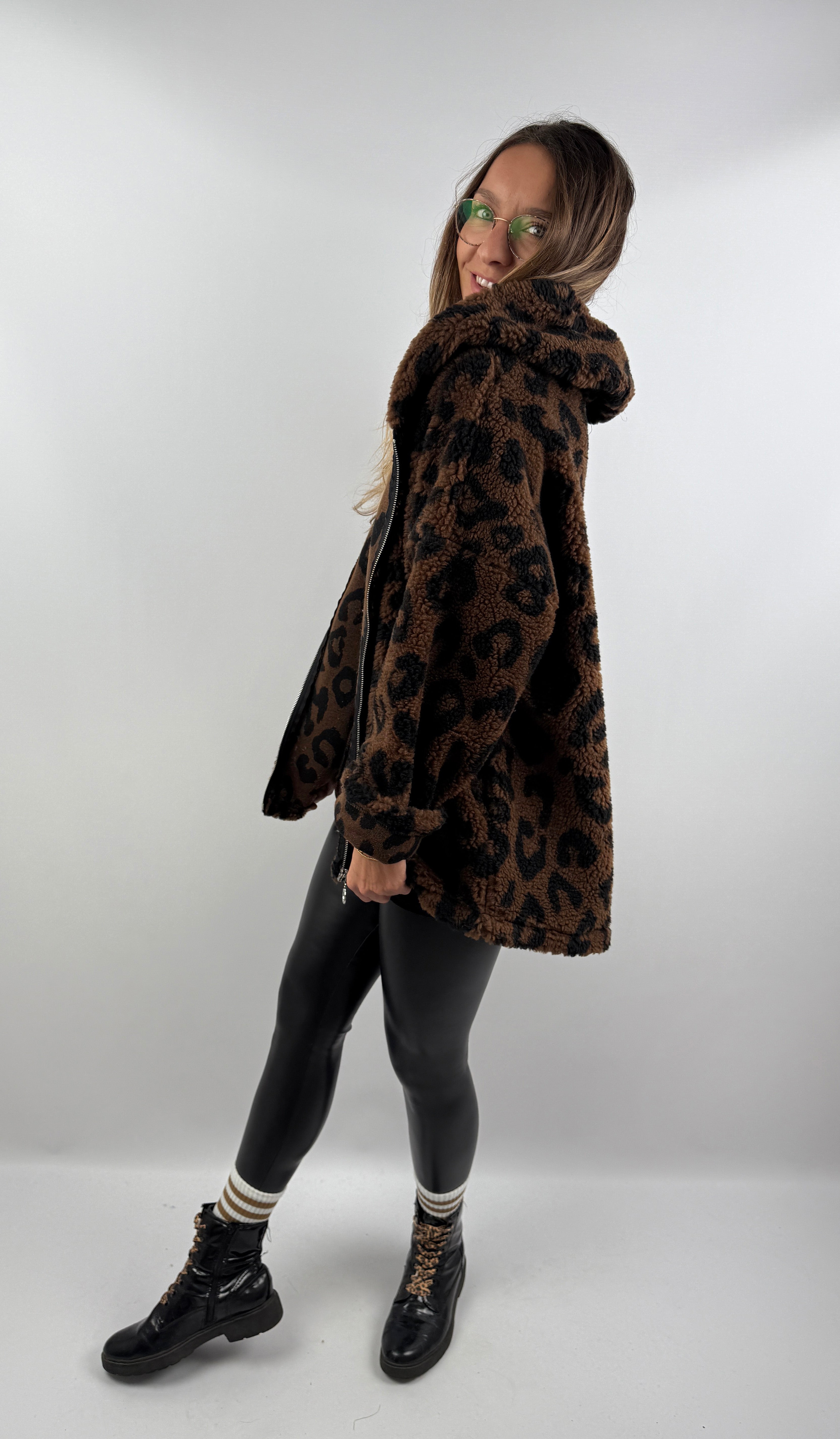 Frau lächelt in einer dunkelbraunen Leo Teddy Jacke mit Leo-Muster und Kapuze, von der Seite fotografiert.