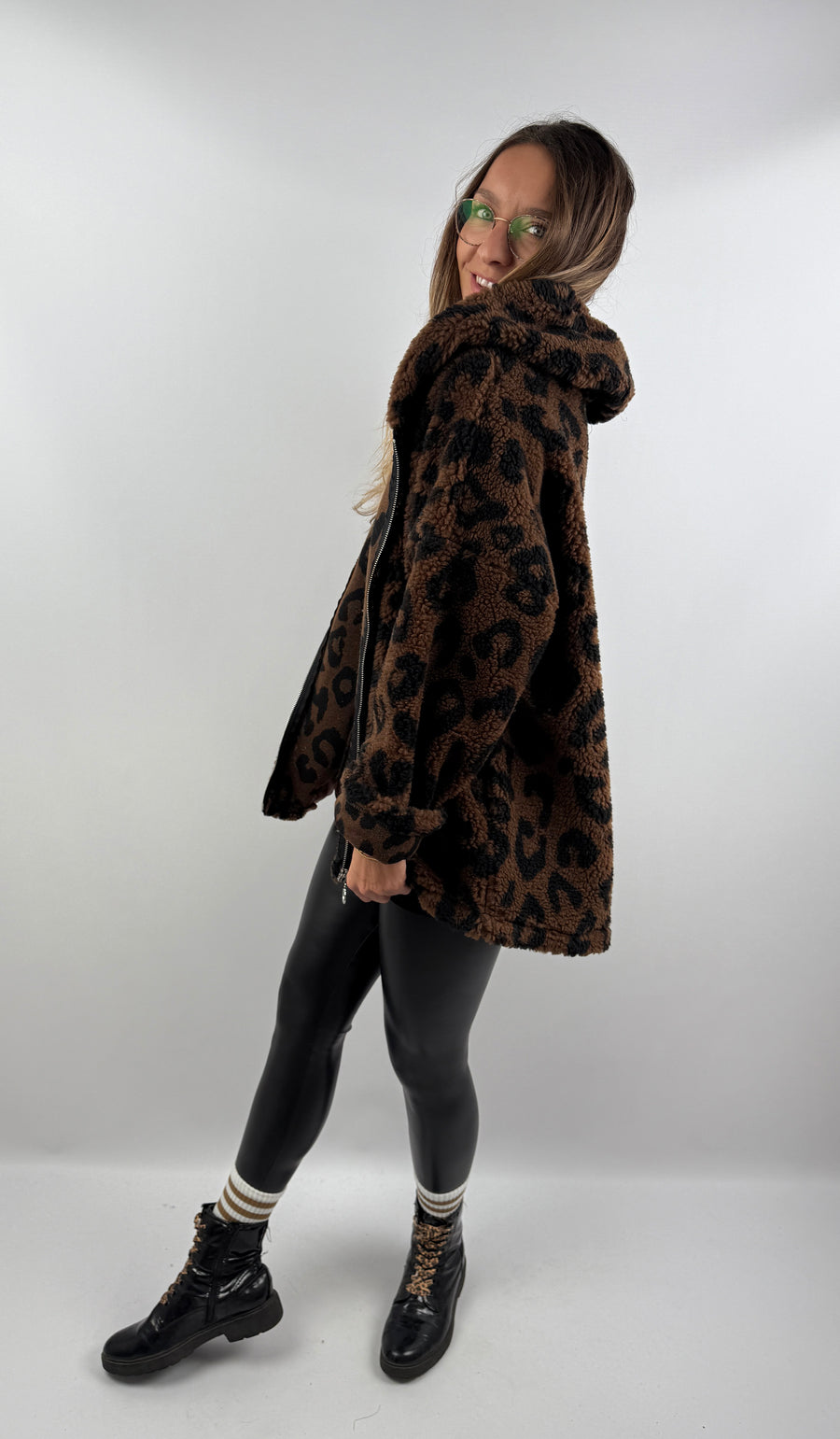 Frau lächelt in einer dunkelbraunen Leo Teddy Jacke mit Leo-Muster und Kapuze, von der Seite fotografiert.
