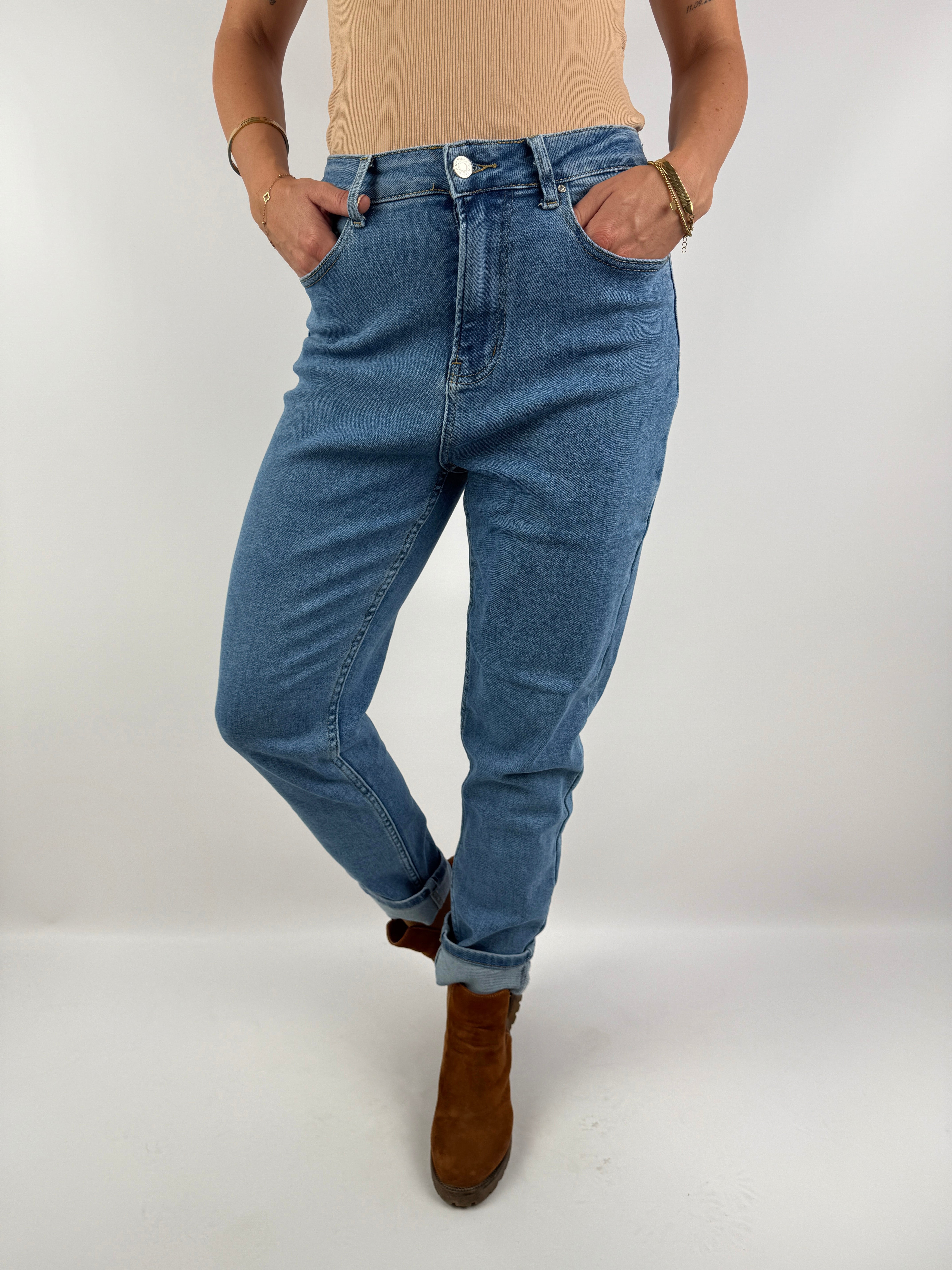 Locker geschnittene Jeans in hellem Denim mit umgeschlagenem Saum, getragen mit braunen Boots und einem beigefarbenen Top – casual Chic Look.