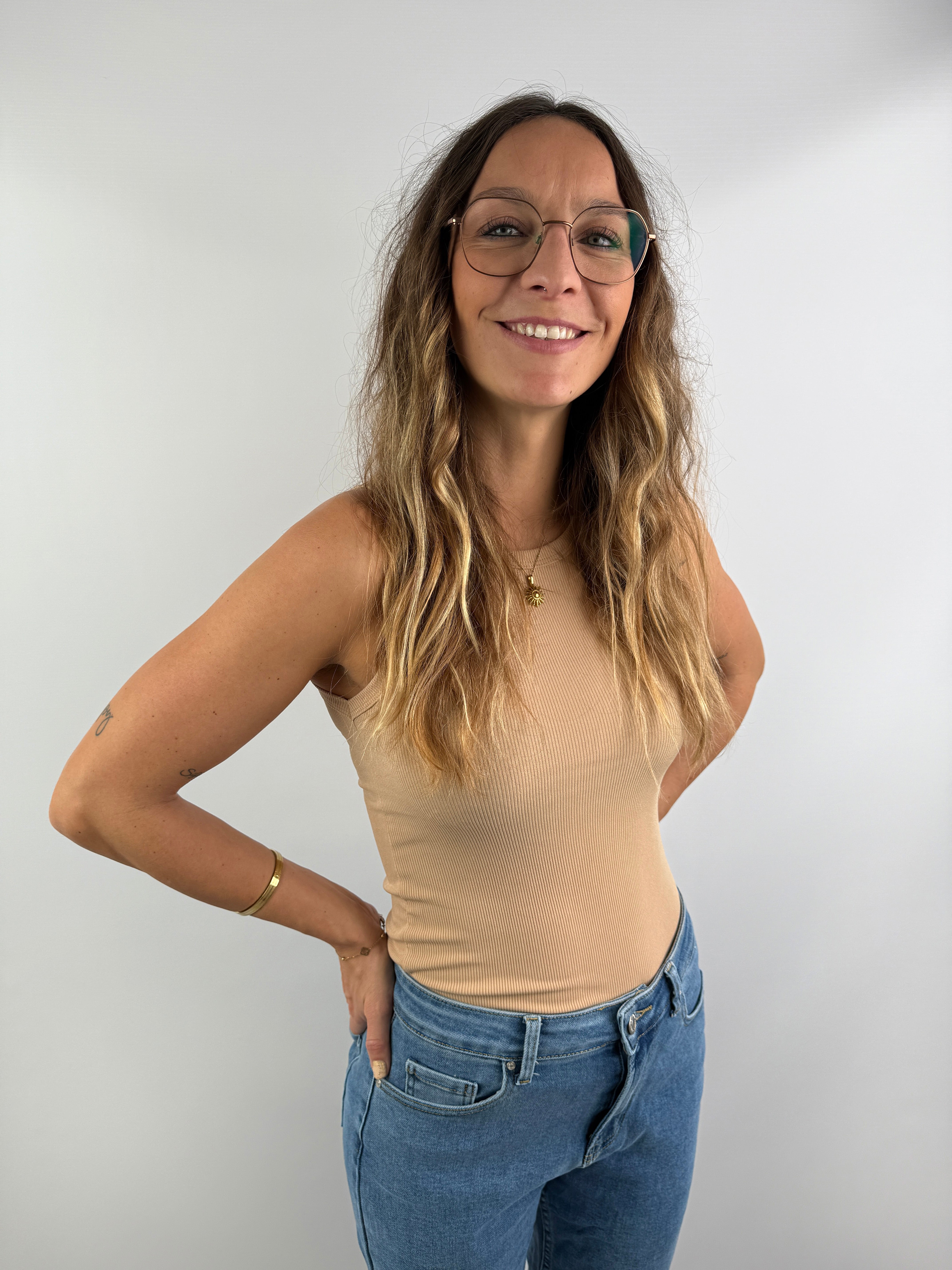 Frau trägt ein beigefarbenes, eng anliegendes Ripp-Top ohne Ärmel, kombiniert mit einer High-Waist-Jeans – clean, modern und feminin.