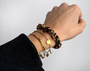 Scrunchie aus Seide im Leopardenmuster als Armband getragen, kombiniert mit goldenen Armreifen – vielseitiges Fashion-Accessoire.
