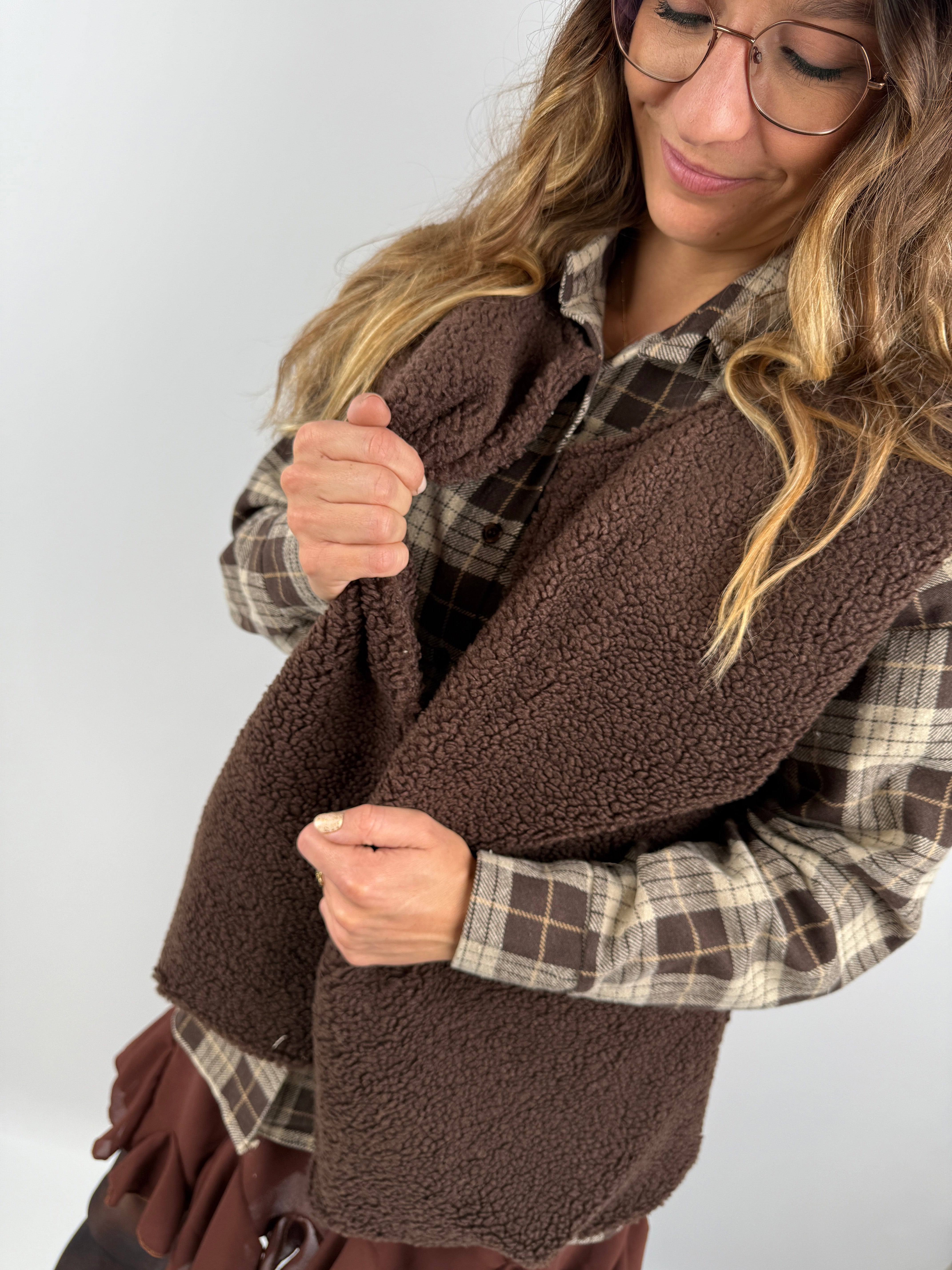 Detailaufnahme einer braunen Fleeceweste in Teddyoptik, kombiniert mit kariertem Hemd – kuscheliger Layering-Look für kühle Tage.