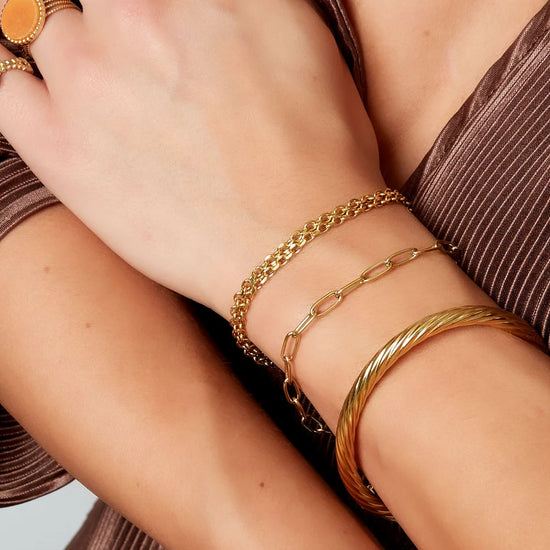 Vergoldetes Edelstahlarmband am Handgelenk kombiniert mit weiterem Goldschmuck