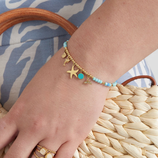 Maritimes Armband mit verschiedenen Perlen in verschiedenen Blautönen und goldenen Perlen und goldenen Anhängern mit Delfin und Seestern.