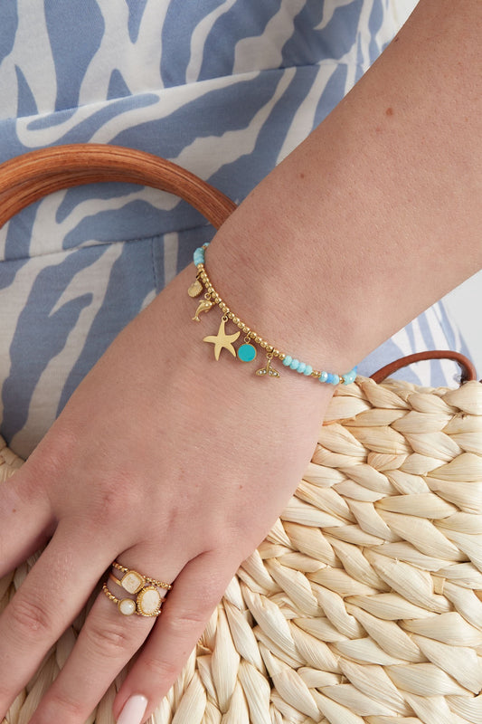 Maritimes Armband mit verschiedenen Perlen in verschiedenen Blautönen und goldenen Perlen und goldenen Anhängern mit Delfin und Seestern.