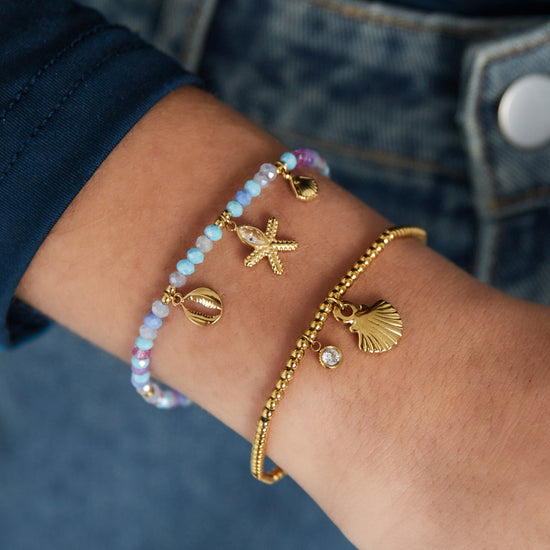 Edelstahl Armband mit Glas und Naturstein Perlen und goldenen Edelstahlanhängern im maritimen Design in pastelligen Lila und Blau Tönen.