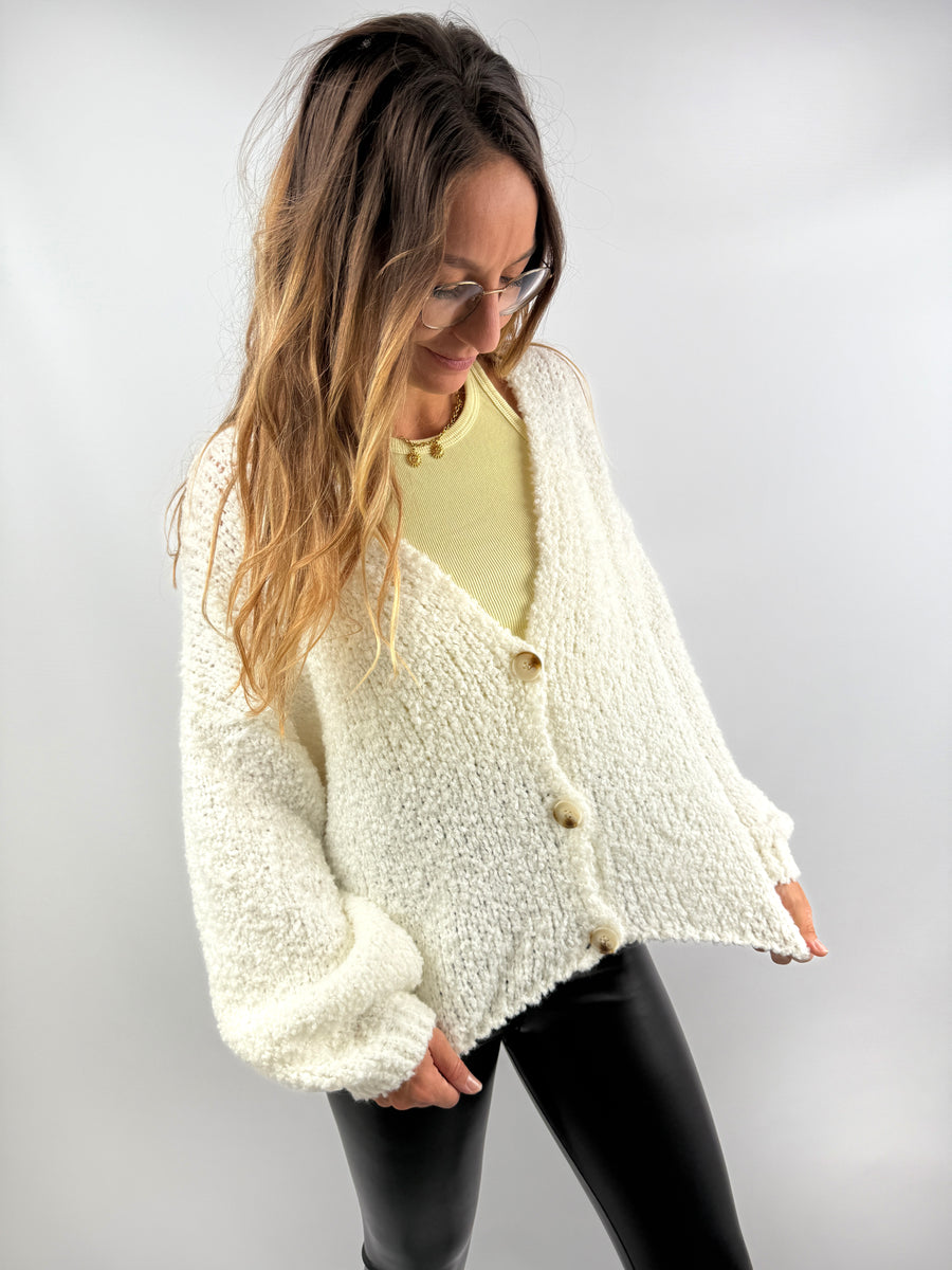 Frau trägt eine weiche cremeweiße Strickjacke mit Knöpfen aus hochwertiger Wollmischung – kombiniert mit einer schwarzen Lederleggings.