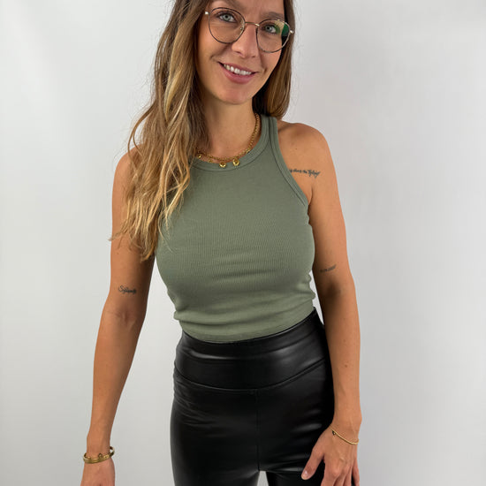 Frau trägt ein olivgrünes, eng anliegendes Ripp-Tanktop mit Rundhalsausschnitt – lässiger Look mit schwarzen Lederleggings.