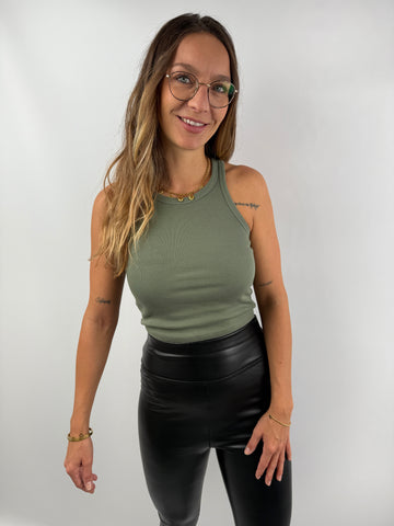 Frau trägt ein olivgrünes, eng anliegendes Ripp-Tanktop mit Rundhalsausschnitt – lässiger Look mit schwarzen Lederleggings.