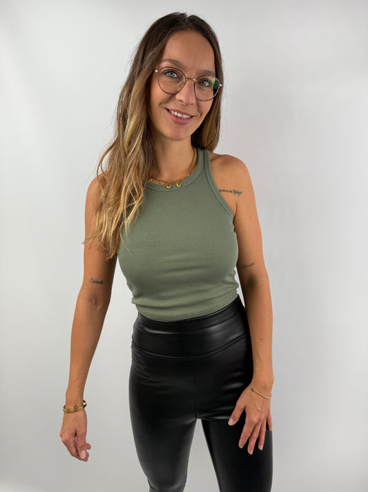 Frau trägt ein olivgrünes, eng anliegendes Ripp-Tanktop mit Rundhalsausschnitt – lässiger Look mit schwarzen Lederleggings.