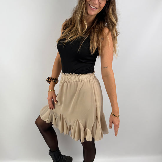 Frau trägt einen beigen Rock mit Volant-Saum und schwarzes Ripp-Top, kombiniert mit schwarzen Boots – moderner, femininer Look mit kontrastreichem Stil.