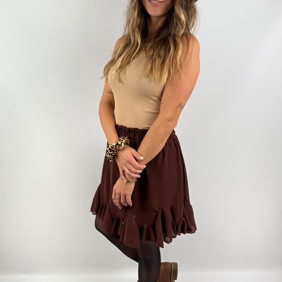 Frau trägt einen braunen Rock mit Volant-Saum, kombiniert mit einem beigefarbenen Ripp-Top, schwarzem Hut und braunen Boots – femininer, herbstlicher Look.