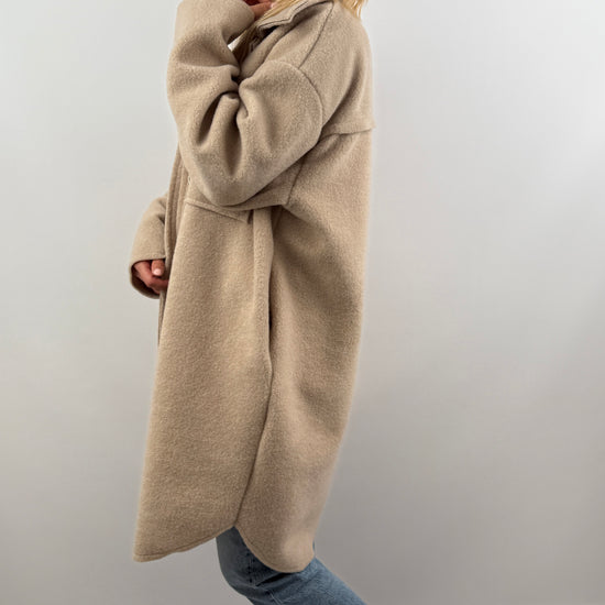 Frau trägt oversized Mantel in Dunkelbraun, seitliche Ansicht, kombiniert mit Jeans und Sneakern.