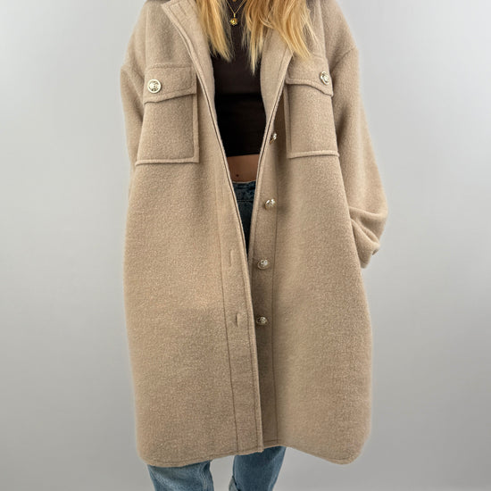 Frau trägt oversized Mantel in Beige, offen über einem dunklen Oberteil, kombiniert mit Jeans.