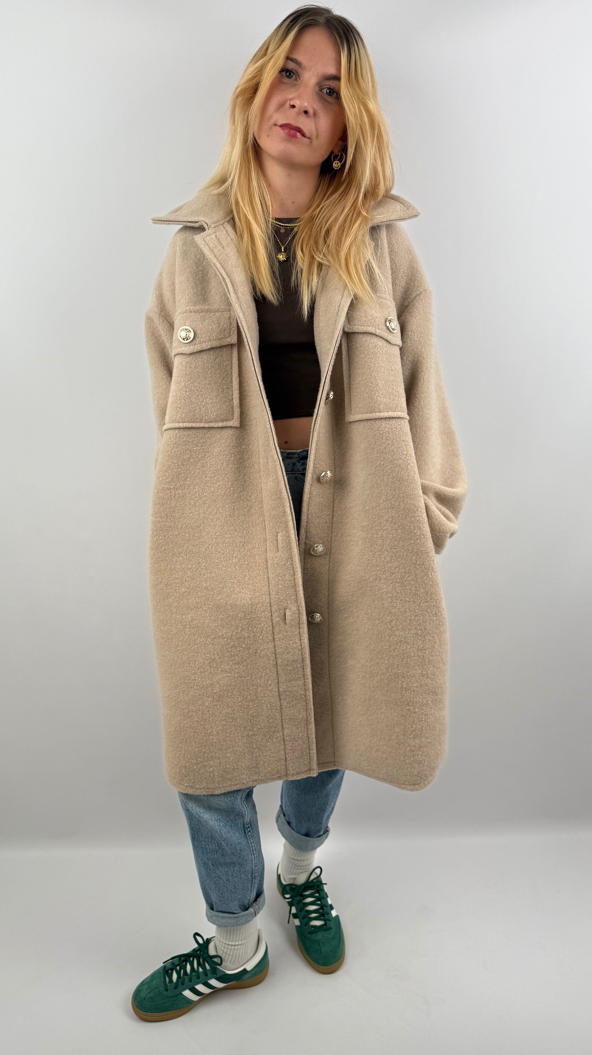 Frau trägt oversized Mantel in Beige, offen über einem dunklen Oberteil, kombiniert mit Jeans.