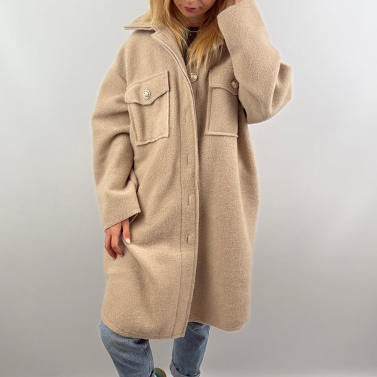 Frau trägt oversized Mantel in Beige, offen über einem dunklen Oberteil, kombiniert mit Jeans.