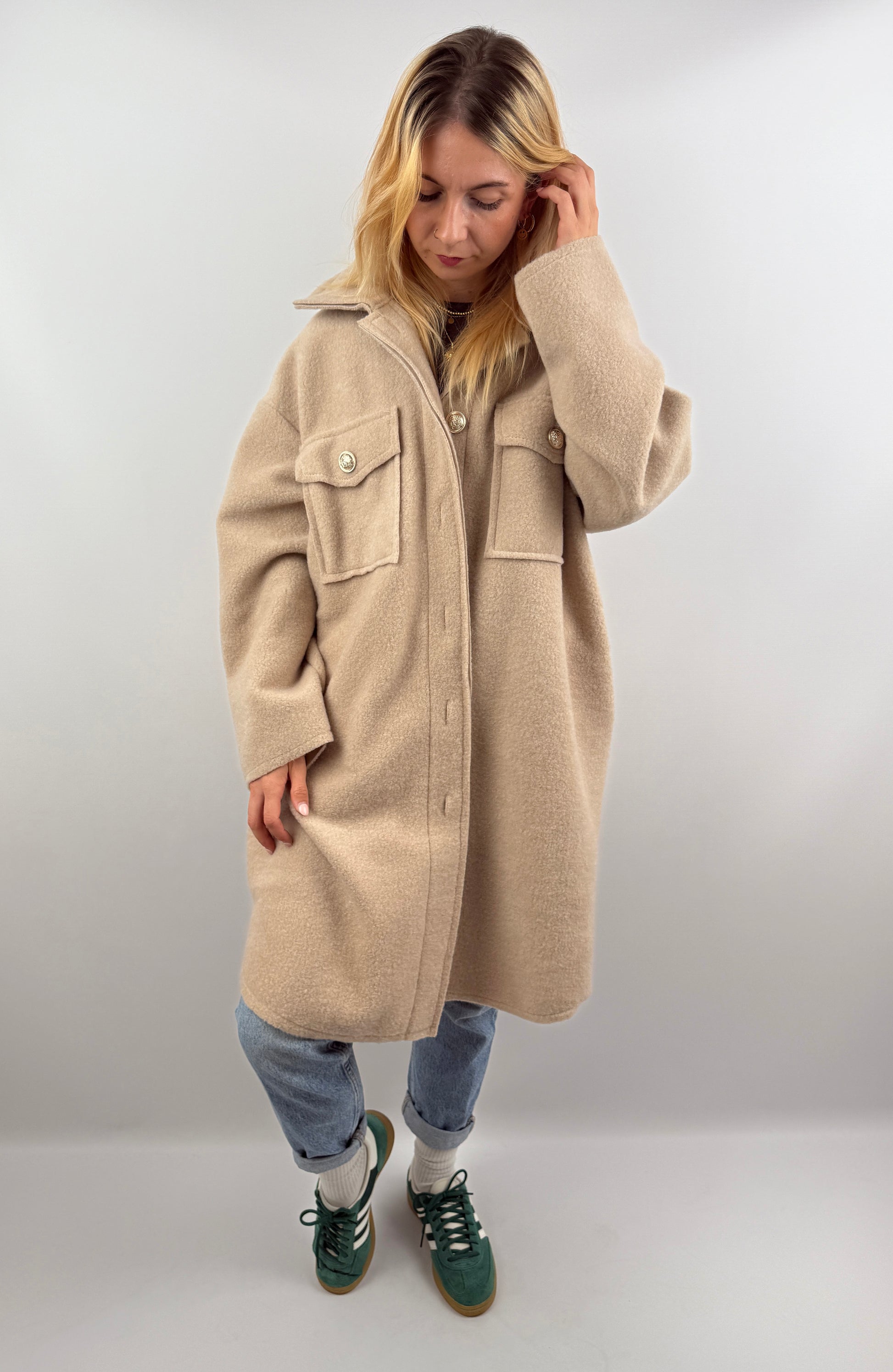 Frau trägt oversized Mantel in Beige, offen über einem dunklen Oberteil, kombiniert mit Jeans.