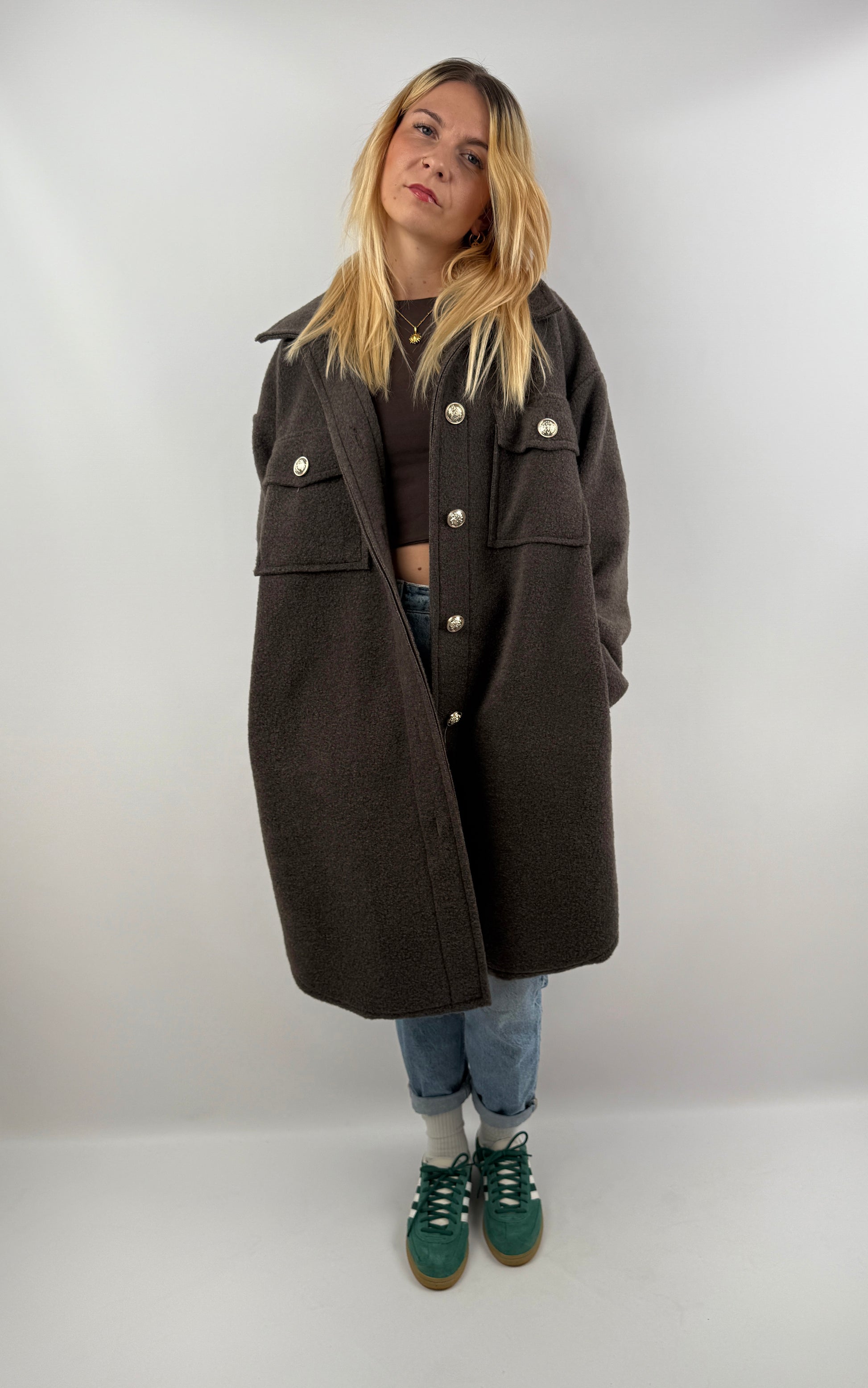 Frau trägt oversized Mantel in Dunkelbraun, kombiniert mit Jeans und grünen Sneakern, herbstliches Outfit.