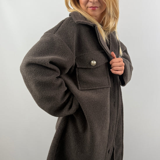 Frau trägt oversized Mantel in Dunkelbraun, seitliche Ansicht, kombiniert mit Jeans und Sneakern.