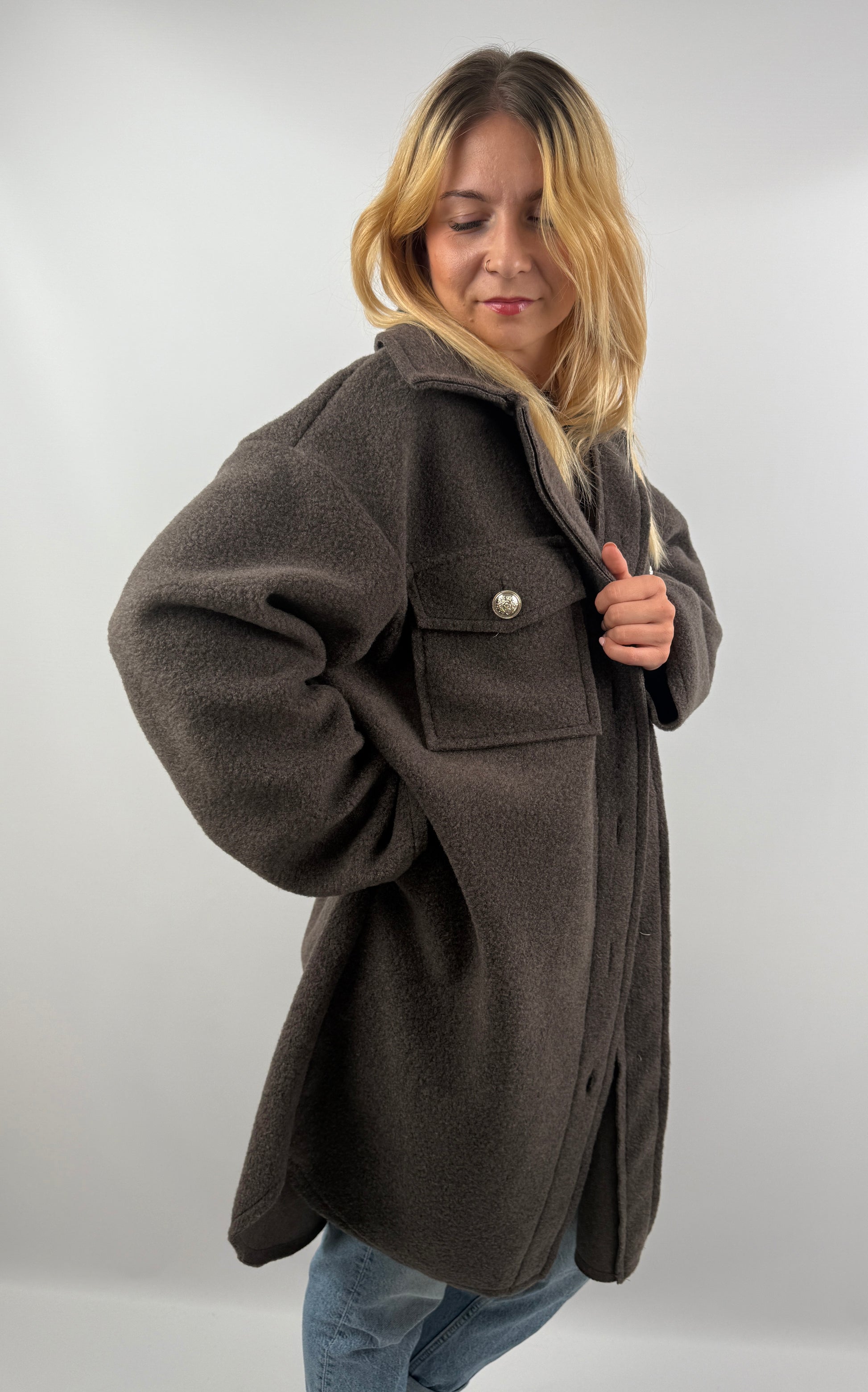 Frau trägt oversized Mantel in Dunkelbraun, seitliche Ansicht, kombiniert mit Jeans und Sneakern.