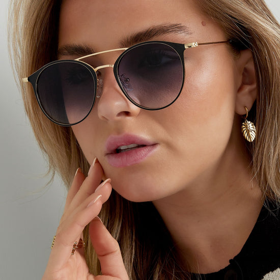 Schwarz goldene Sonnenbrille mit schwarzen Brillengläsern und roten Enden.