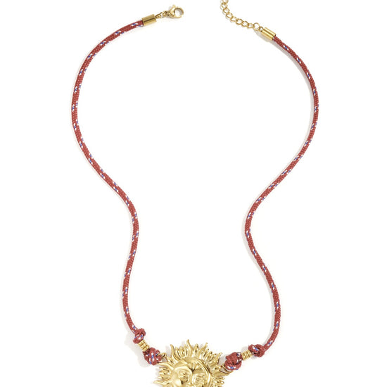 Vergoldeter Edelstahl-Sonnenanhänger an rotem Band auf weißem Hintergrund.