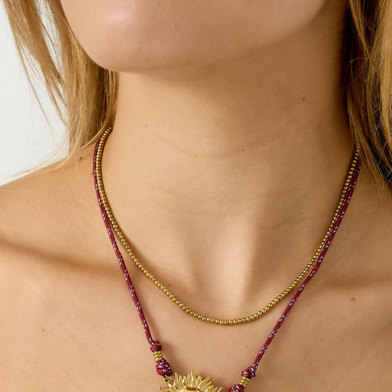 Detailaufnahme der vergoldeten Edelstahl-Sonnenkette mit rotem Band.