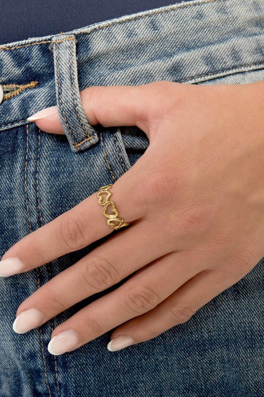 Hand mit goldfarbenem Edelstahl-Herzring, getragen zu Jeans.