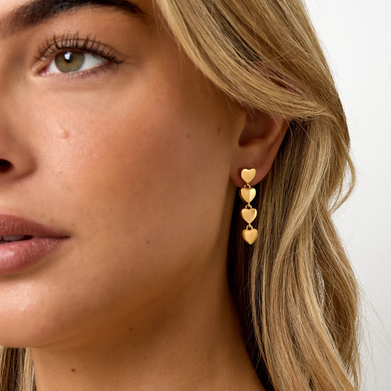 Goldene Herz-Ohrhänger am Ohr einer Frau, Nahaufnahme.