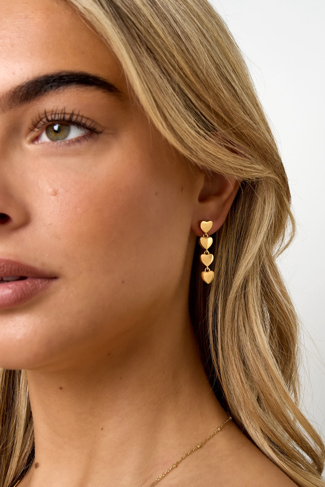 Goldene Herz-Ohrhänger am Ohr einer Frau, Nahaufnahme.