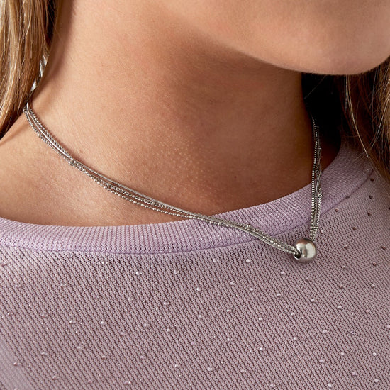 Versilberte mehrreihige Edelstahlkette mit Kugelanhänger an einer Frau, Nahaufnahme.