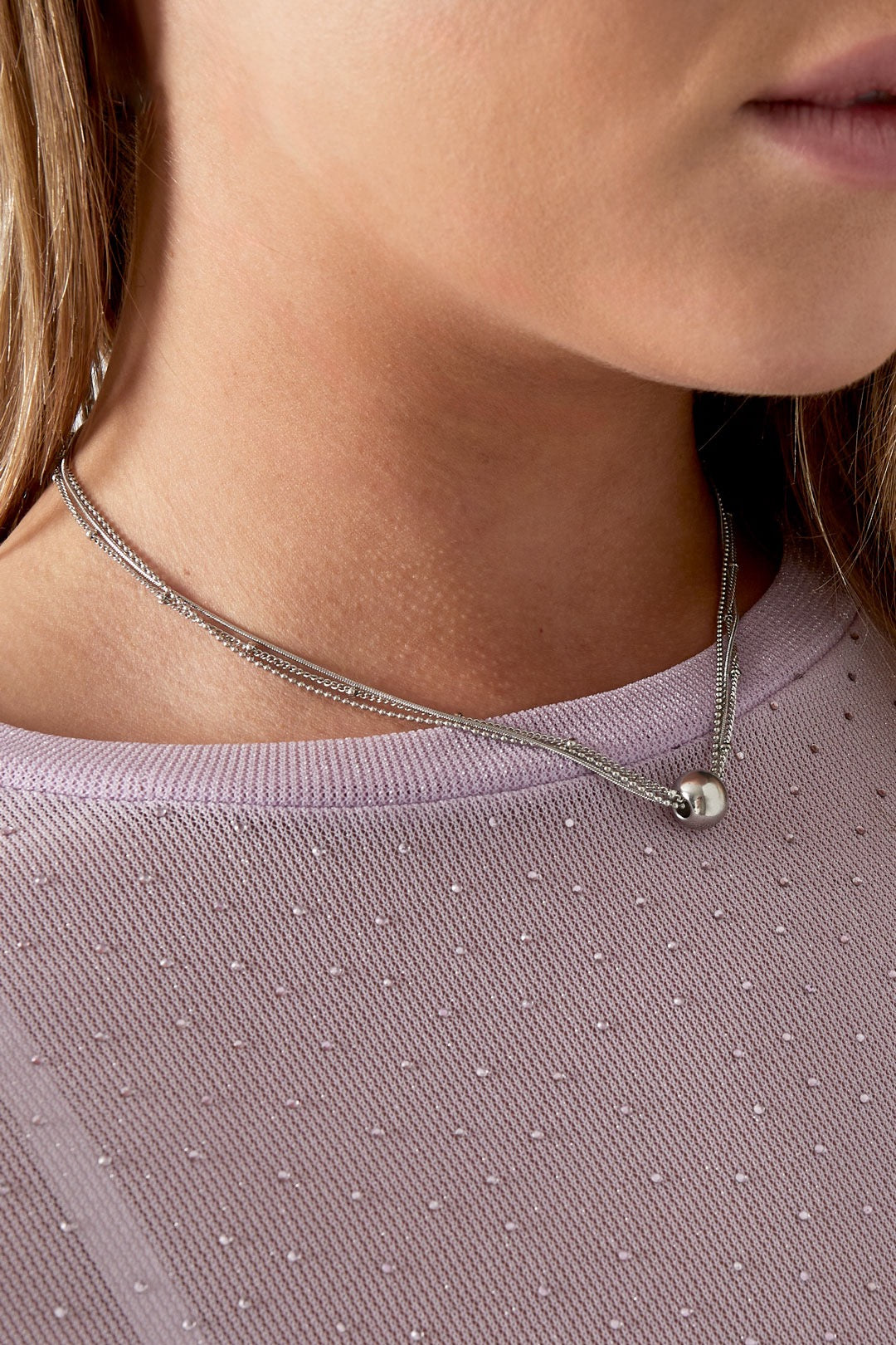 Versilberte mehrreihige Edelstahlkette mit Kugelanhänger an einer Frau, Nahaufnahme.