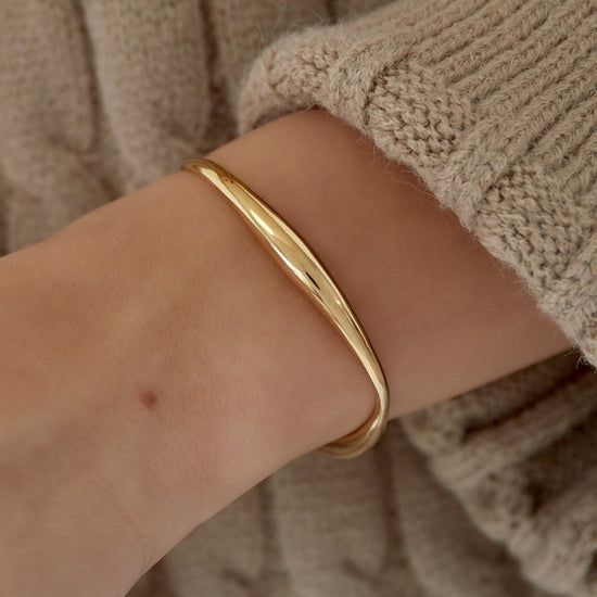 Goldfarbener Edelstahl Armreif am Handgelenk kombiniert mit beigem Strickpullover