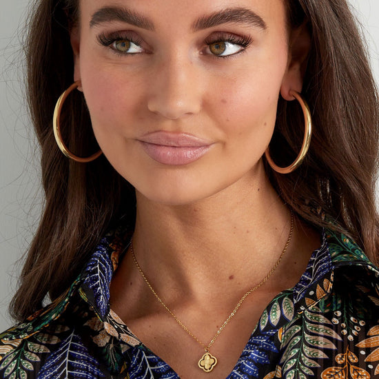 Frau mit goldener Kleeblatt-Kette, kombiniert mit großen Creolen.