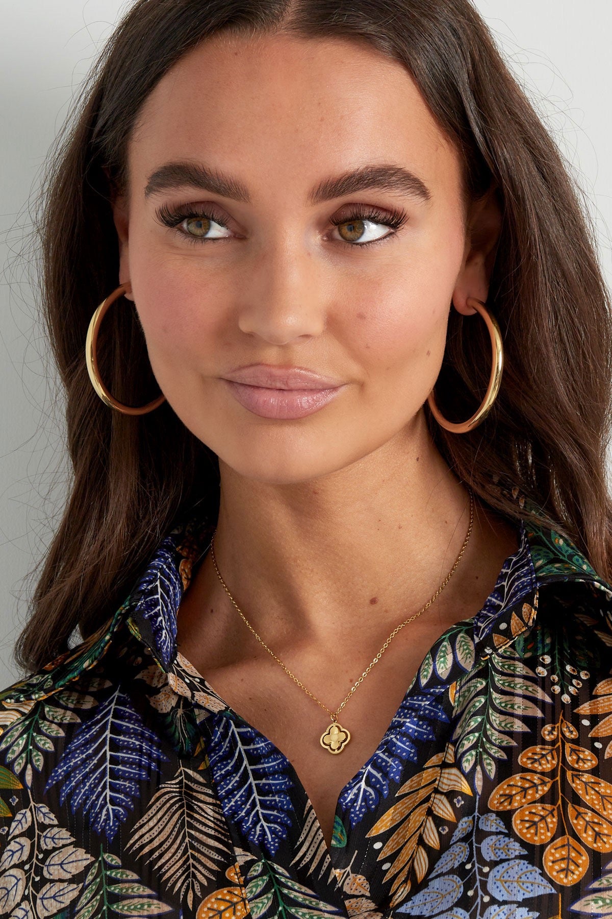 Frau mit goldener Kleeblatt-Kette, kombiniert mit großen Creolen.