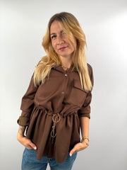 Frau trägt braune Jacke mit Taillenzug, kombiniert mit Jeans und Sneakern.