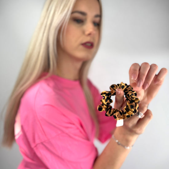 Frau präsentiert einen seidenen Leoparden-Haargummi vor der Kamera.
