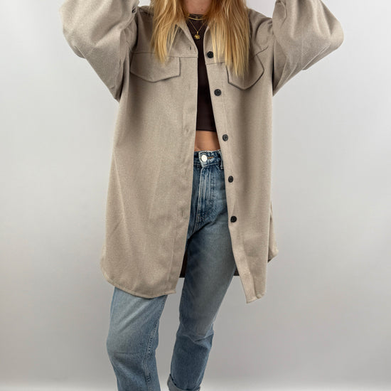 Frau trägt beige Long Hemd Jacke offen über Jeans und Crop Top.
