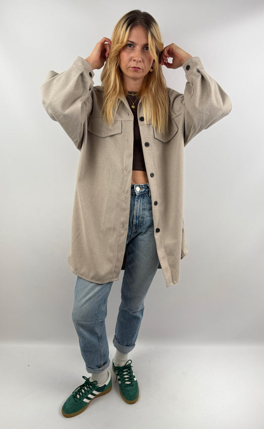 Frau trägt beige Long Hemd Jacke offen über Jeans und Crop Top.