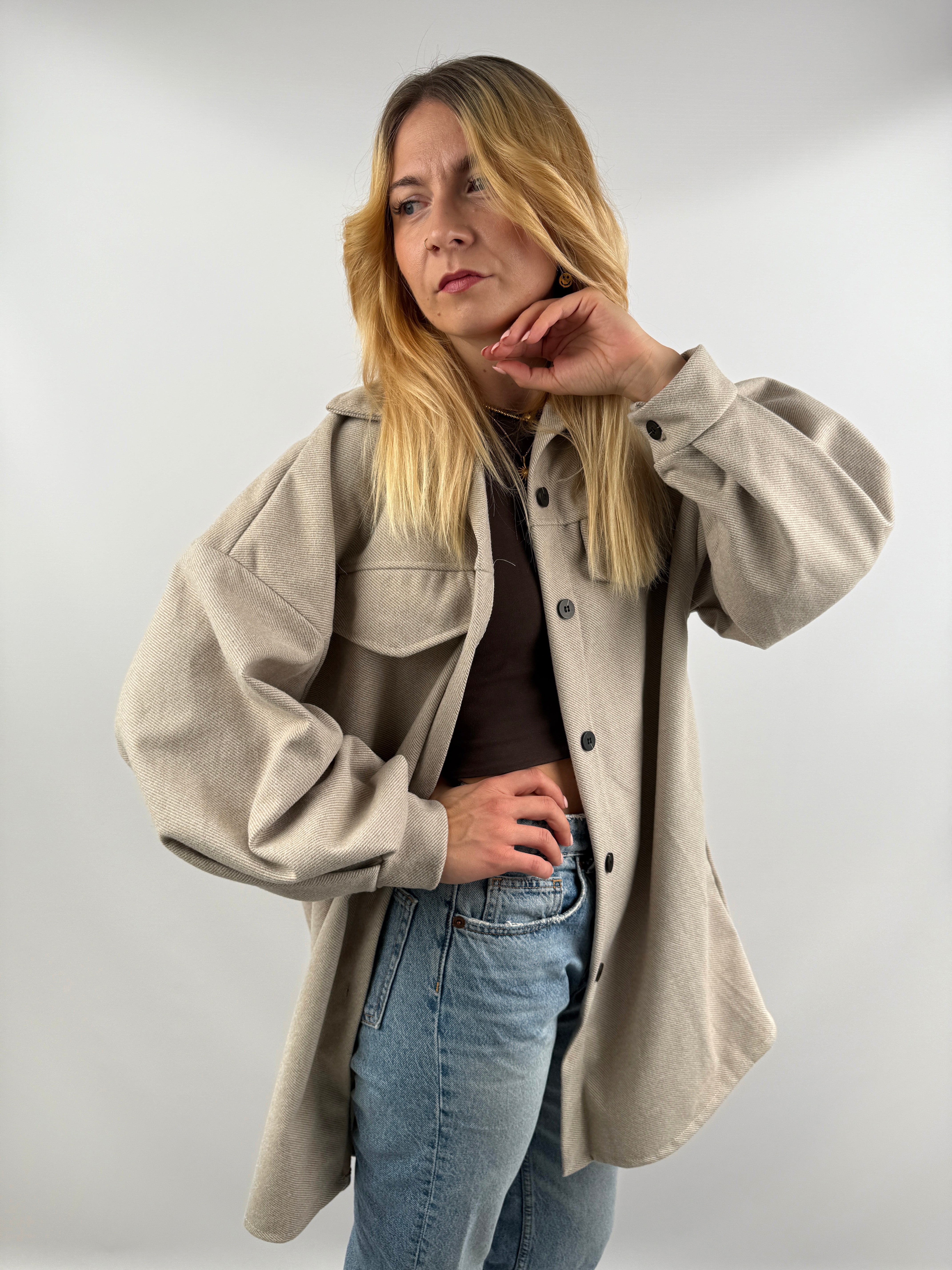 Frau trägt beige Long Hemd Jacke seitlich, mit Jeans kombiniert.