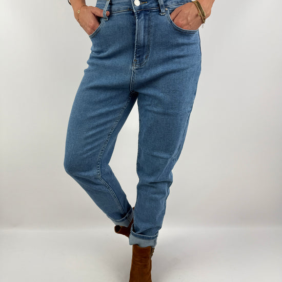 Locker geschnittene Jeans in hellem Denim mit umgeschlagenem Saum, getragen mit braunen Boots und einem beigefarbenen Top – casual Chic Look.