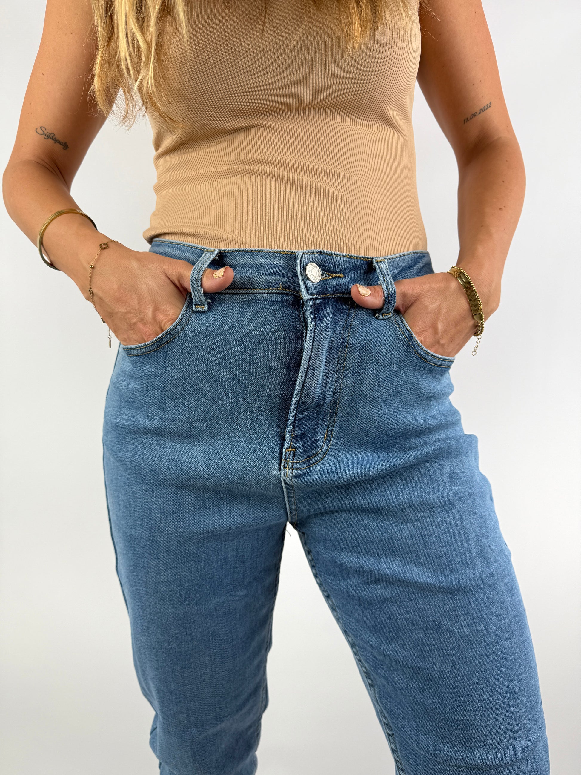 Nahaufnahme einer hellblauen High-Waist-Jeans mit klassischem Schnitt, kombiniert mit einem beigefarbenen Ripp-Top – clean und modern gestylt.