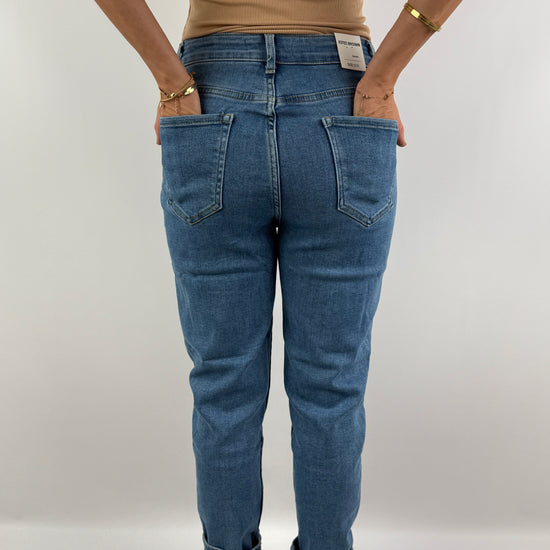 Rückenansicht einer figurbetonten High-Waist-Jeans in hellblauem Denim, kombiniert mit einem beigefarbenen Top – lässig und zeitlos.