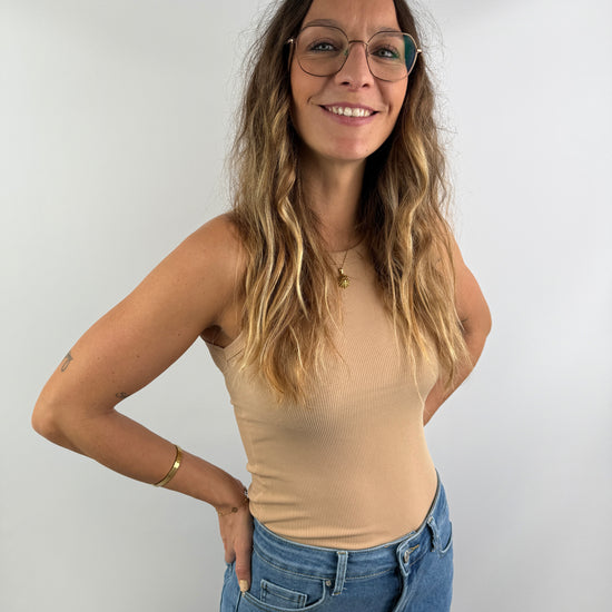 Frau trägt ein beigefarbenes, eng anliegendes Ripp-Top ohne Ärmel, kombiniert mit einer High-Waist-Jeans – clean, modern und feminin.