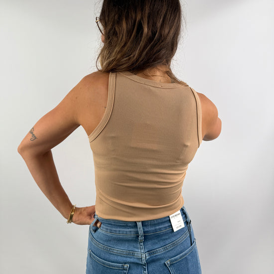 Rückenansicht eines beigefarbenen, gerippten Tanktops aus weichem Stretchmaterial, getragen zu einer hellblauen Jeans – schlicht und elegant.
