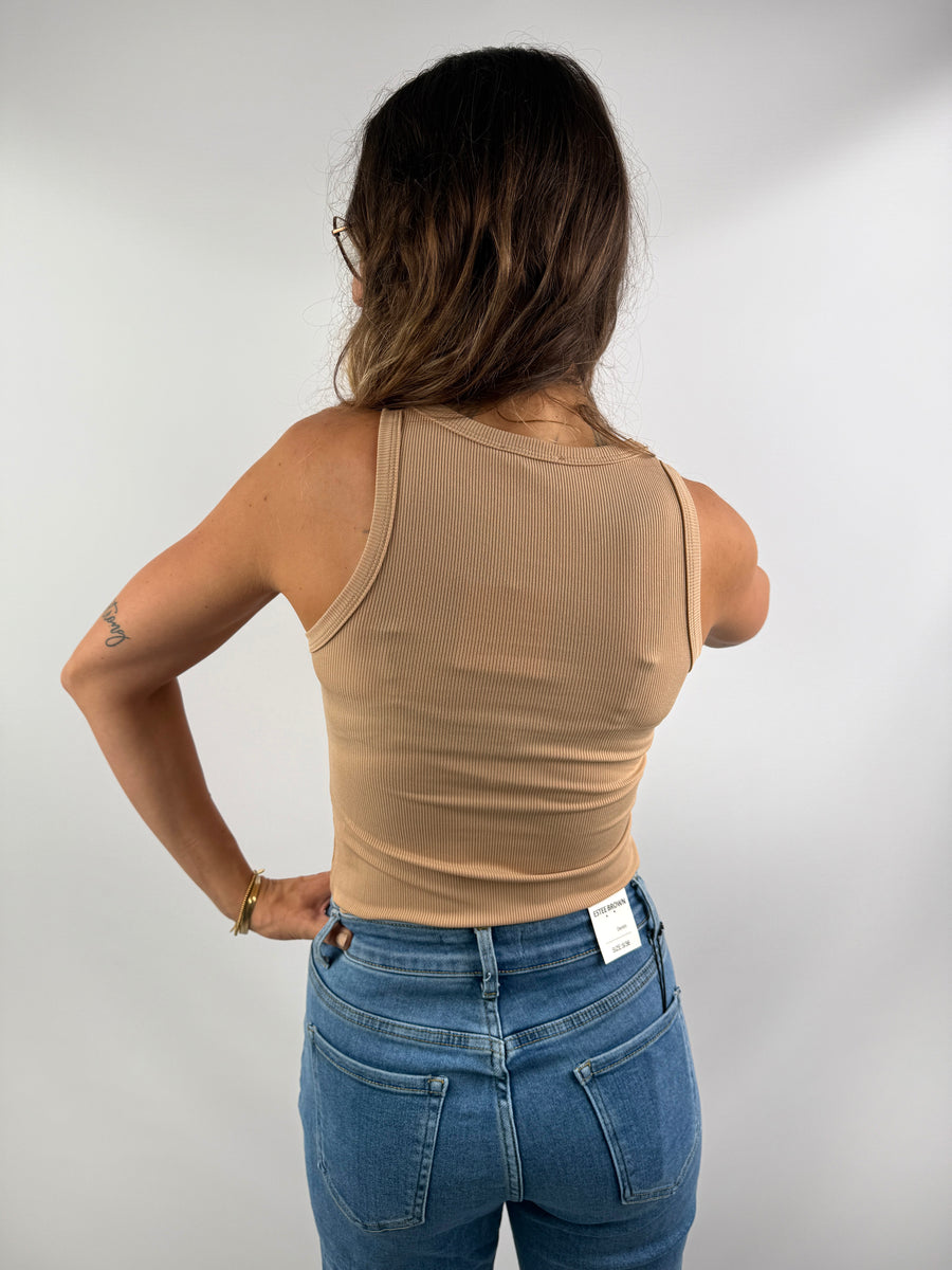 Rückenansicht eines beigefarbenen, gerippten Tanktops aus weichem Stretchmaterial, getragen zu einer hellblauen Jeans – schlicht und elegant.
